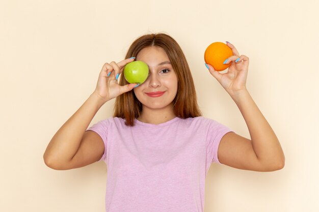 Front view young attractive female in pink t-shirt and blue jeans holding apple orange and posing