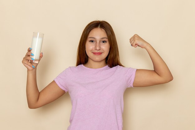 Front view young attractive female in pink t-shirt and blue jeans holding glass of milk and flexing