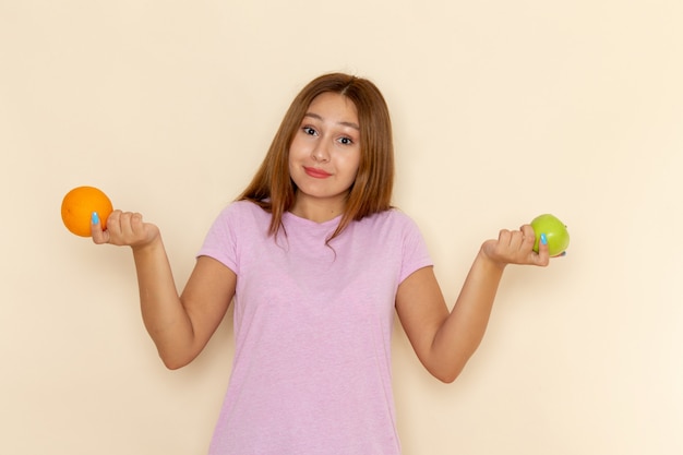 Front view young attractive female in pink t-shirt and blue jeans holding orange and apple