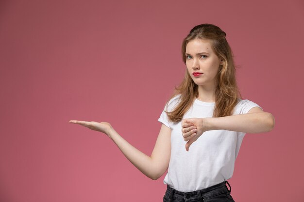 Front view young attractive female showing unlike sign with displeased expression on dark-pink wall model color female young girl