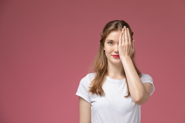 Front view young attractive female smiling covering half of her face on pink wall model color female young