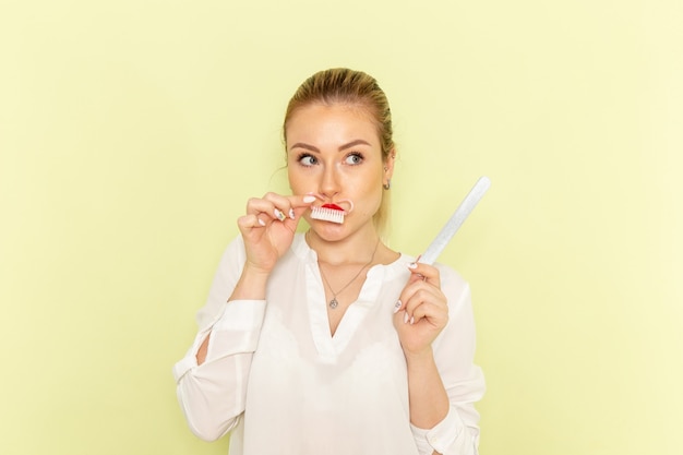 Front view young attractive female in white shirt fixing her nails on light-green surface