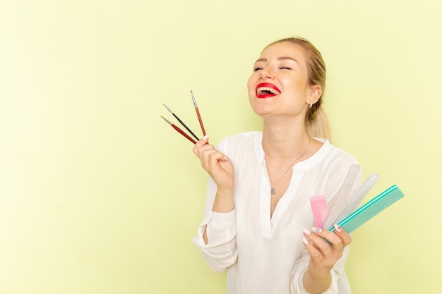 Front view young attractive female in white shirt holding tassels and manicure accessories on green surface