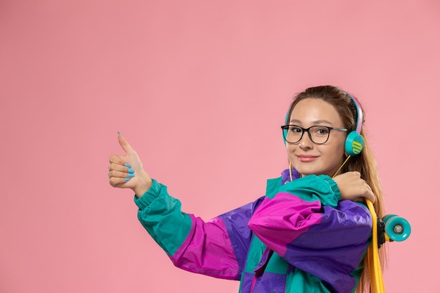 Free photo front view young attractive female in white t-shirt colored coat holding skateboard with a slight smile on the pink background