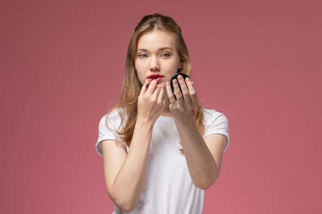 Front view young attractive female in white t-shirt doing make-up on pink wall model color female young girl