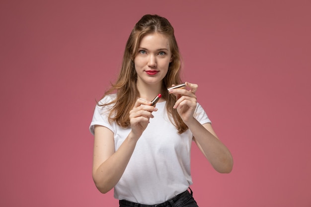 Front view young attractive female in white t-shirt holding lipstick on the dark-pink wall model color female young girl