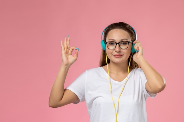 Free photo front view young attractive female in white t-shirt listening to music with earphones and smile on the pink background