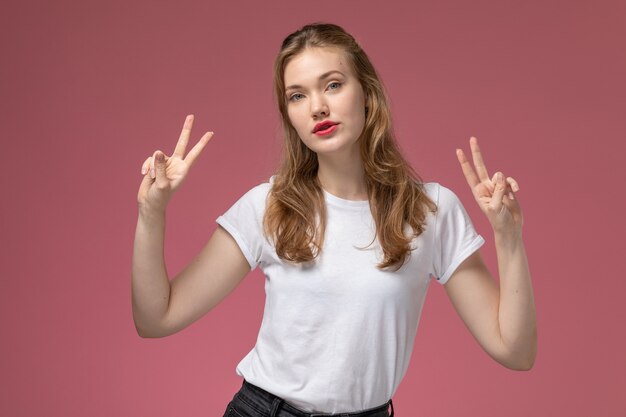 Front view young attractive female in white t-shirt posing showing victory sign on pink wall model female pose color photo female young