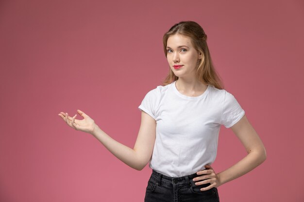 Front view young attractive female in white t-shirt posing with hand gesture smiling on pink wall model color female young