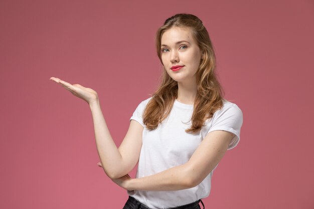 Front view young attractive female in white t-shirt posing with hand gestures on the pink wall model female pose color photo