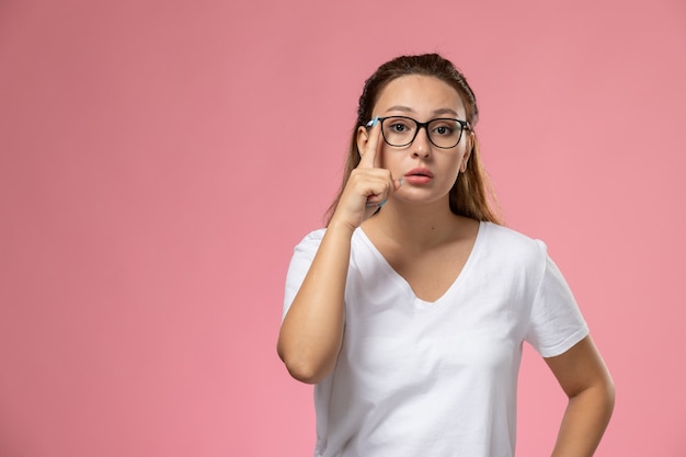 Front view young attractive female in white t-shirt posing with optical sunglasses on the pink background