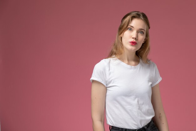 Front view young attractive female in white t-shirt posing with surprised expression on pink wall model female pose color female young