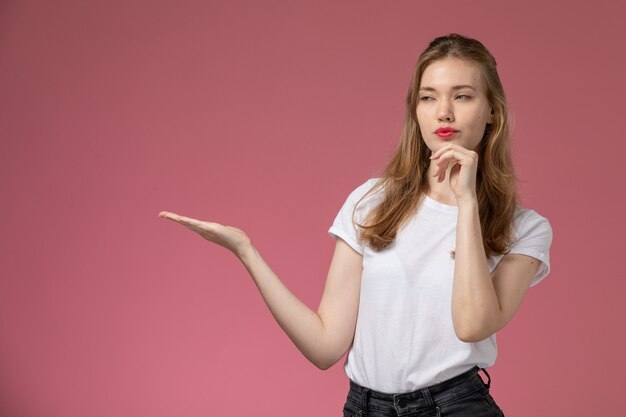 Front view young attractive female in white t-shirt posing with thinking expression on pink wall model female pose color photo