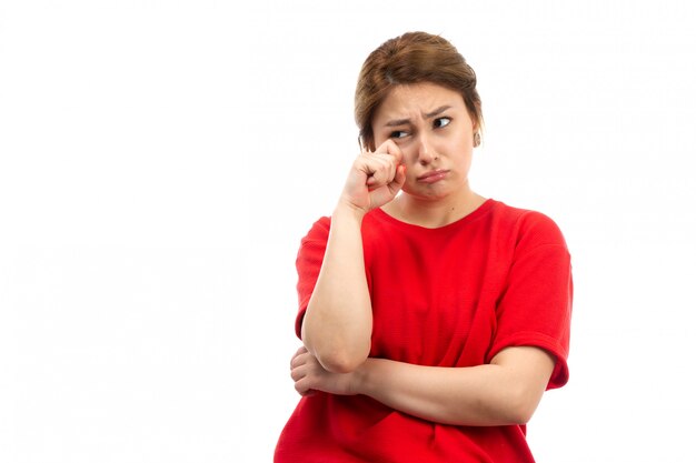 A front view young attractive girl in red t-shirt wearing black jeans crying emotions on the white