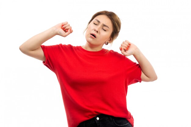 A front view young attractive girl in red t-shirt wearing black jeans wanting to sleep sneezing on the white