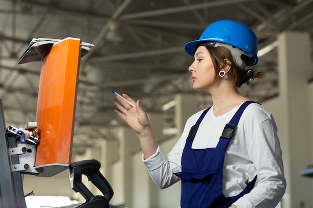 Free photo a front view young attractive lady in blue construction suit and helmet controlling machines in hangar during daytime buildings architecture construction