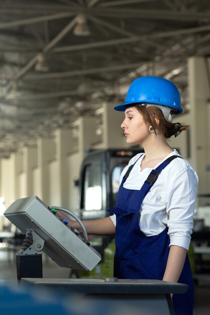 A front view young attractive lady in blue construction suit and helmet controlling machines in hangar working during daytime buildings architecture construction