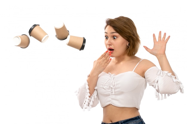 A front view young attractive lady in white shirt and blue jeans throwing coffee cups surprised on the white