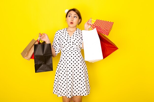 A front view young beautiful female in black and white polka dot dress holding shopping packages on yellow