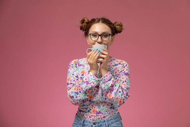 Free photo front view young beautiful female in flower designed shirt and blue jeans drinking a tea smiling on pink background