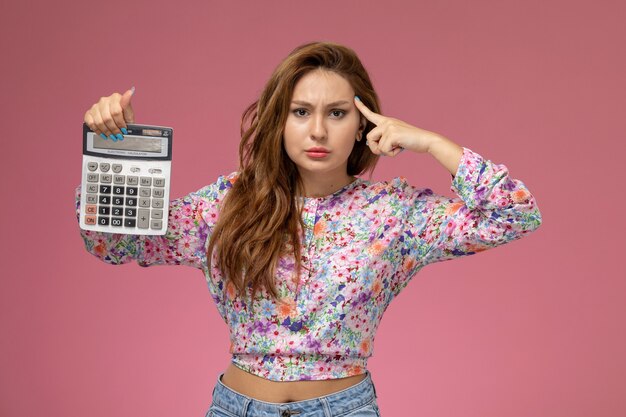 Free Photo front view young beautiful female in flower designed shirt and blue jeans holding calculator on pink background