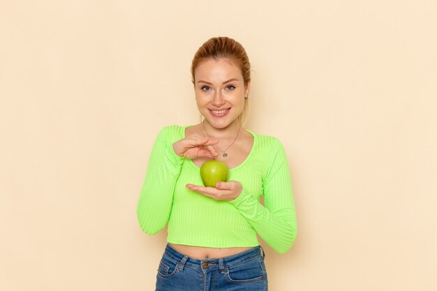 Front view young beautiful female in green shirt holding green fresh apple on cream wall fruit model woman