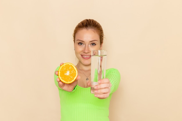 Free Photo front view young beautiful female in green shirt holding orange slice and glass of water on the cream wall fruit model woman mellow