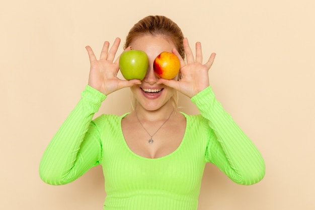 Free photo front view young beautiful female in green shirt holding pair of fresh apples covering her eyes on cream wall fruit model woman mellow