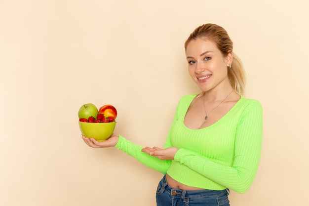 Free Photo front view young beautiful female in green shirt holding plate full of fruits on the light cream wall fruit model woman pose