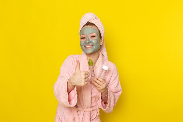 A front view young beautiful female in pink bathrobe holding sprays and smiling