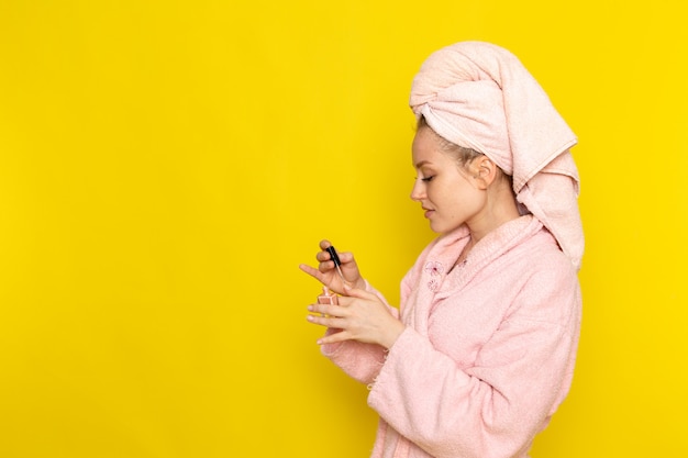 Free photo a front view young beautiful female in pink bathrobe using nail polish