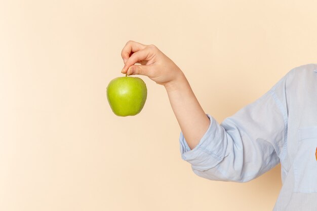 Front view young beautiful female in shirt holding fresh green apple on the cream wall fruit model woman pose