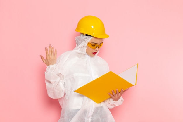 Free photo front view young beautiful female in special white suit wearing protective helmet holding yellwo file on the pink space special suit  woman