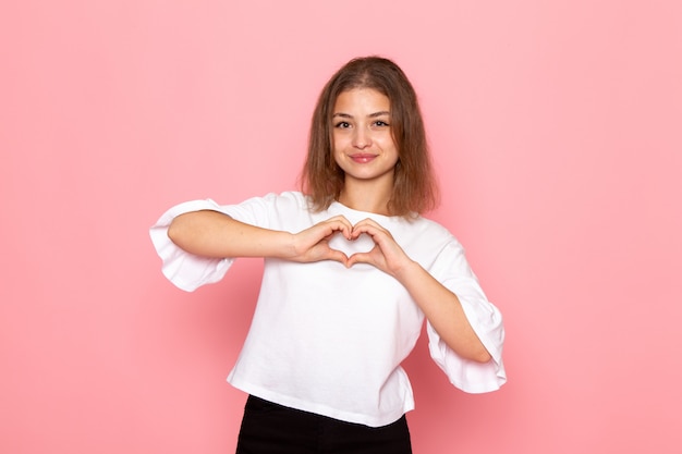 A front view young beautiful female in white shirt smiling and showing heart shape