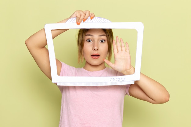 Free Photo a front view young beautiful girl in pink t-shirt posing with white tv shaped paper on green