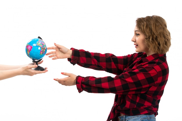 Free photo a front view young beautiful girl in red-black checkered shirt and blue jeans taking little globe on the white