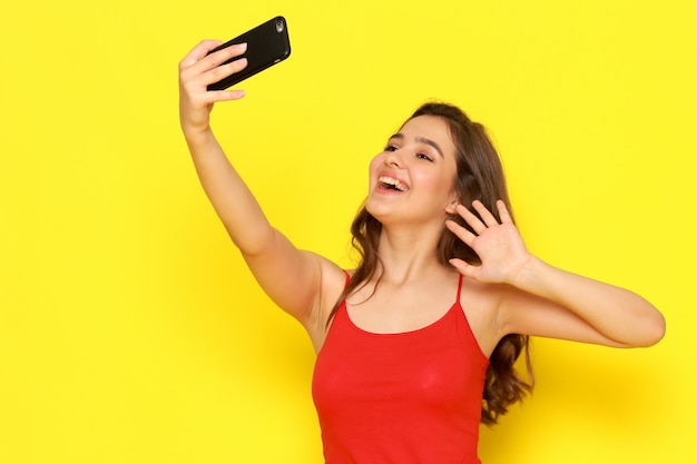 A front view young beautiful girl in red shirt and blue jeans taking a selfie with smile