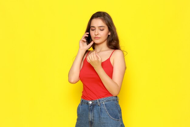 A front view young beautiful girl in red shirt and blue jeans talking on the phone