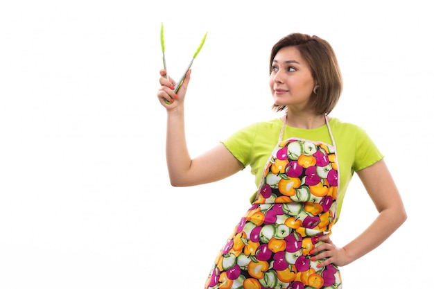 Free photo a front view young beautiful housewife in green shirt colorful cape holding green kitchen appliance smiling on the white background house cleaning kitchen