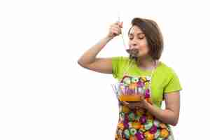 Free photo a front view young beautiful housewife in green shirt colorful cape mixing liquid eggs preparing meal trying on the white background house female kitchen