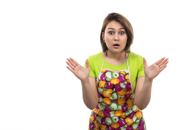 A front view young beautiful housewife in green shirt colorful cape posing shocked expression on the white background house female kitchen