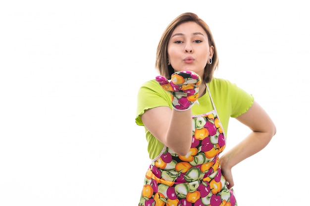 A front view young beautiful housewife in green shirt colorful cape sending air kisses on the white background house cleaning kitchen