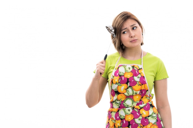 A front view young beautiful housewife in green shirt colorful cape smiling holding kitchen appliance thinking on the white background house cleaning kitchen