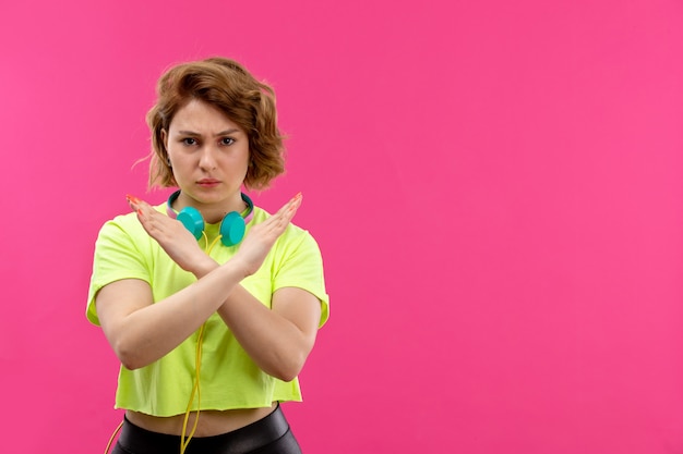 Free Photo a front view young beautiful lady in acid colored shirt black trousers with blue earphones showing banned sign