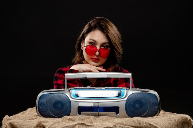 Free photo a front view young beautiful lady in checkered red-black shirt in red sunglasses posing with tape-recorder