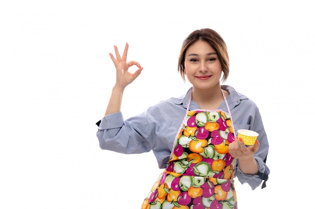 A front view young beautiful lady in light blue shirt and colorful cape holding yellow cake pans happy smiling expression