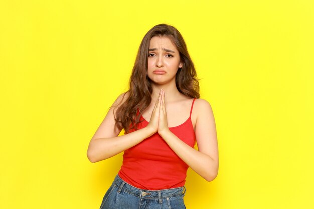 A front view young beautiful lady in red shirt and blue jeans posing with begging expression