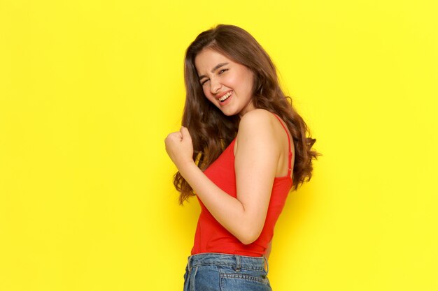 A front view young beautiful lady in red shirt and blue jeans posing with delighted expression