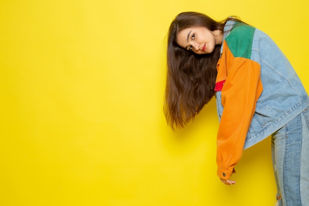 A front view young beautiful lady in red shirt colorful coat and blue jeans posing