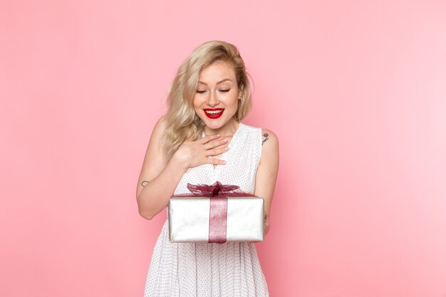 A front view young beautiful lady in white dress holding present box with smile on her face